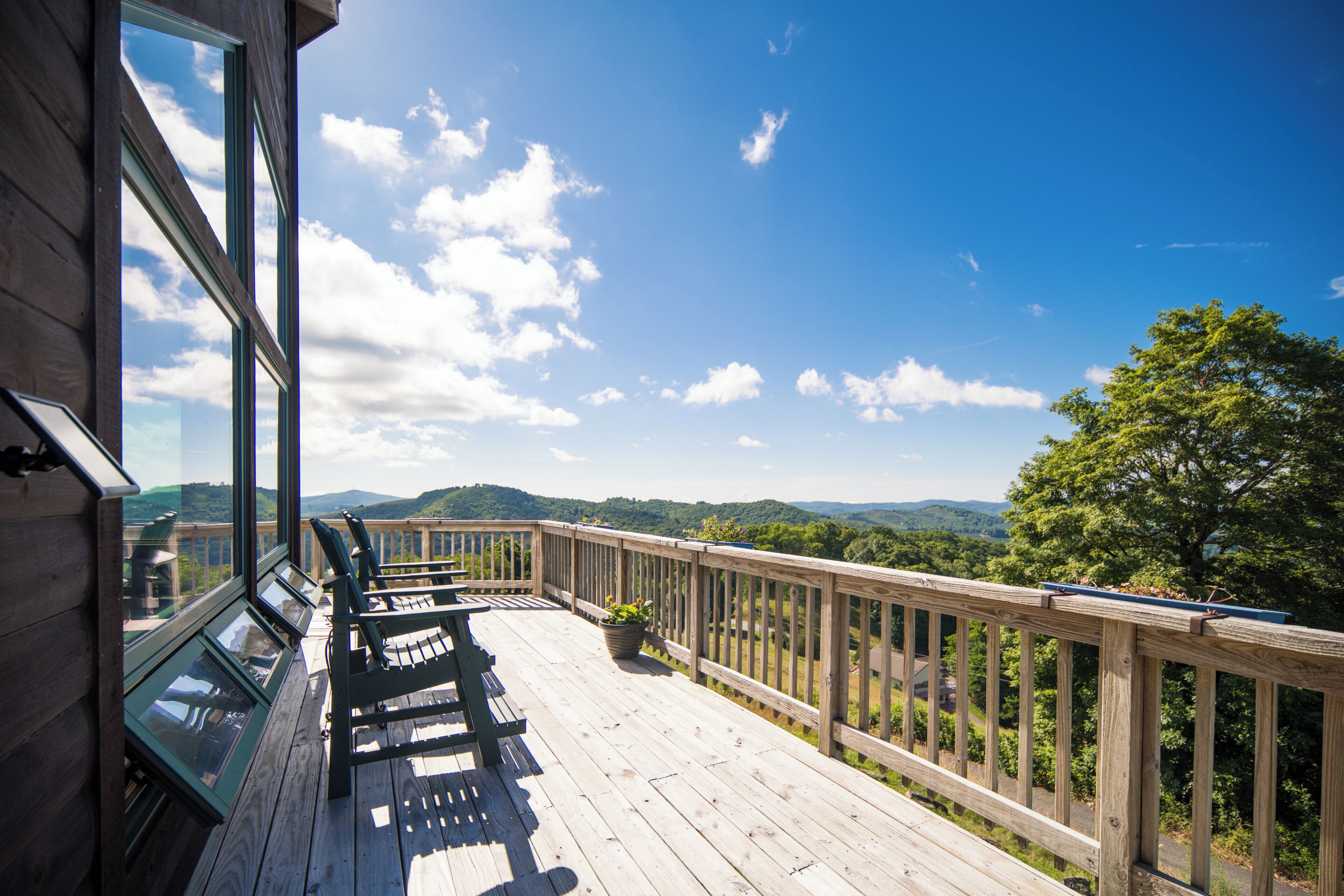 A wooden deck with a view of the landscape, a railing, and a bench.