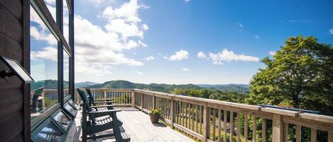 A wooden deck with a view of the landscape, a railing, and a bench.