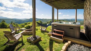 Un espace extérieur aménagé avec un jacuzzi, des fauteuils Adirondack, un hamac et un mur en pierre.