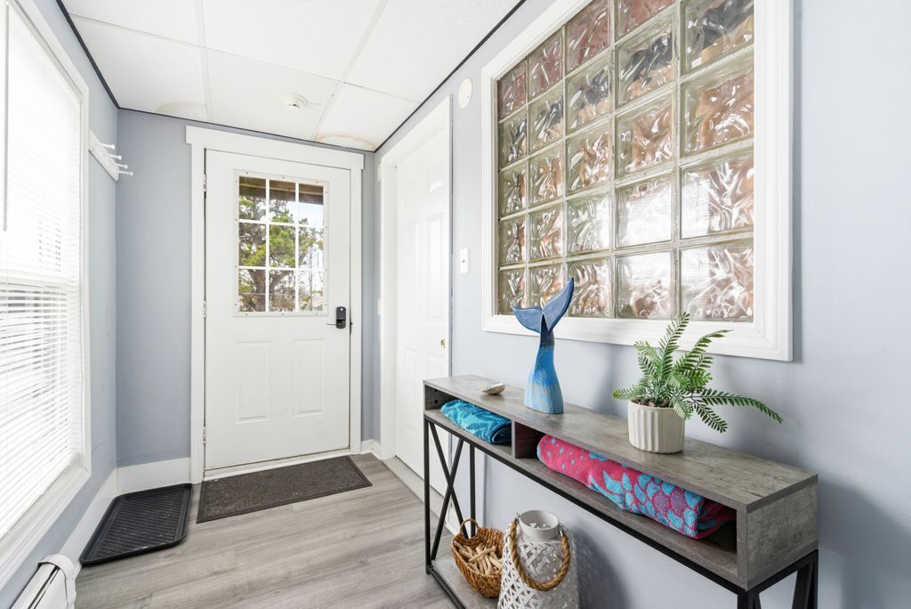 A hallway with a white door, a window with a grid pattern, a console table with a vase and plant, and a wooden floor.