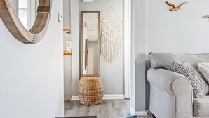 Ein Wohnzimmer mit grauem Sofa, Wandbehagung aus Makramee, einem gewebten Korb und einem spiegelnden Holzrahmen.