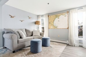 Una sala de estar con un sofá, otomanas, un mapa en la pared y una lámpara.