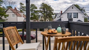 Eine Holzterrasse mit zwei Stühlen, einem kleinen runden Tisch und einem Metallkessel.