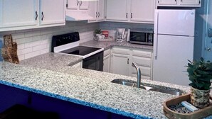 A kitchen with white cabinets, a granite countertop, a stove, a microwave, and a sink. - POOL, PARKING, 2BR 2 BA, walk to town! (Rehoboth Beach)