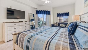 Un dormitorio con cama, cómoda, televisor, ventilador de techo y balcón con vistas.