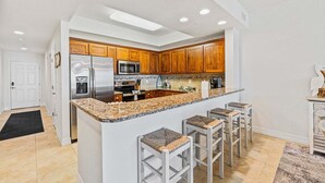 Una cocina moderna con encimeras de granito, electrodomésticos de acero inoxidable, armarios de madera y una isla central con taburetes de bar.