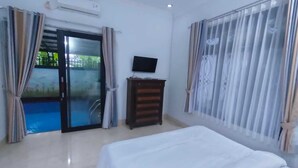 Une chambre d’hôtel avec un lit, une télévision, une commode en bois et une porte-fenêtre coulissante donnant sur une piscine.