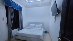 Une petite chambre à coucher, bien rangée, avec un lit, des rideaux, un téléviseur et une porte.