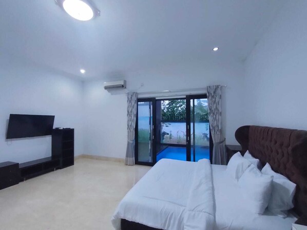 Un dormitorio con cama, televisor y puerta corrediza de vidrio que da a un balcón.