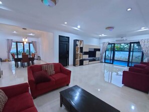 Amplia sala de estar con un sofá rojo, una mesa de centro negra y un mueble para la televisión. Se encuentra un comedor con una mesa y sillas, y un ventanal con vistas al exterior.