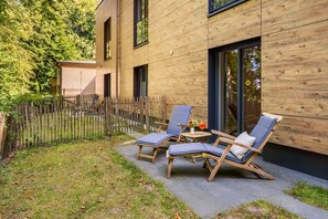A modern building with a wooden facade, a fenced garden area, and outdoor seating with cushions.