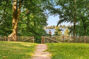 A pathway leading to a body of water, surrounded by trees and a wooden fence. - Vacation apartment with three terraces between the forest and the lake (Ratzeburg)