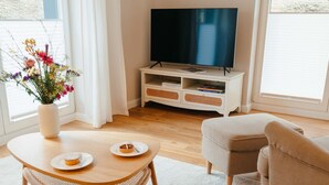 A modern living room with a flat-screen TV, a round coffee table with two plates, a beige sofa, and a white cabinet with a TV stand. - The vacation apartment with three terraces is located between the forest and the lake (Ratzeburg)