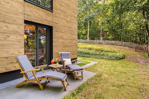 A modern outdoor seating area with wooden furniture and a glass door leading to a garden. - Vacation apartment with three terraces between the forest and the lake (Ratzeburg)