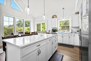 A modern kitchen with a large island, white cabinetry, and pendant lighting. - Beach House Chalet - shared access to Rangeley Lake (Rangeley)