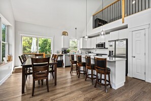 Uma cozinha moderna com armários brancos, uma ilha central e uma área de refeições com cadeiras de madeira.