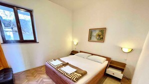 Une chambre à coucher avec un lit en bois, du linge de lit blanc, un parquet en chevrons, une fenêtre et un tableau au mur.