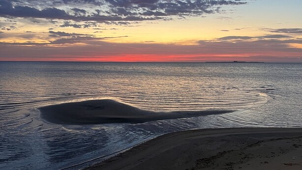 A beach with a calm sea and a sunset.