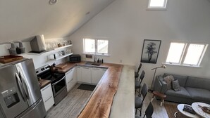A modern kitchen with a long island, stainless steel appliances, and a dining area with a gray sofa and coffee table.
