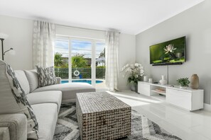 A modern living room with a sofa, coffee table, and TV. - Pompano Collection - Sleeps 16, close to beach (Pompano Beach)