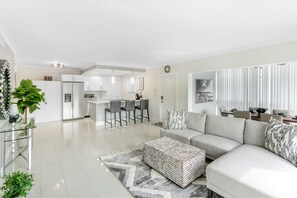 Uma sala de estar moderna com um sofá modular, uma mesa de centro de vidro e uma cozinha ao fundo.