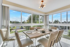 Uma área de refeições com uma mesa posta para quatro pessoas, janelas amplas e um lustre.