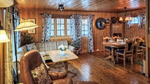 A cozy cabin interior with a wooden ceiling, a dining area with a table and chairs, and a sofa with floral cushions. - Midtholmen by Interhome (Konsmo)