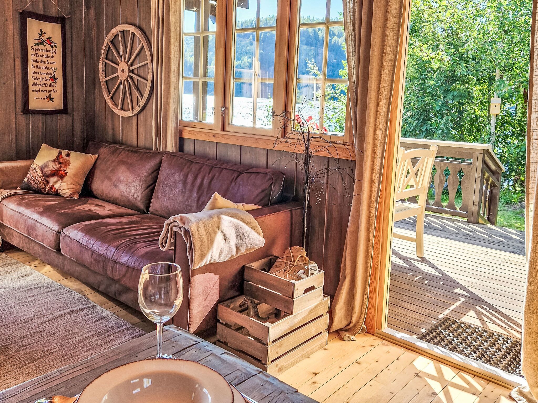 Une pièce chaleureuse avec un canapé en cuir, une table en bois sur laquelle se trouve un verre à vin, et une fenêtre donnant sur un paysage verdoyant.