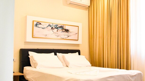 A modern hotel room with a large bed, a nightstand, a wall-mounted air conditioner, and a framed abstract painting. - Hotel Delmar (Golem)