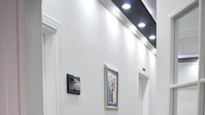 A hallway with white walls, a marble floor, and a door with a glass panel. - Hotel Delmar (Golem)
