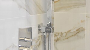 A bathroom with a marble wall, a shower with a handheld showerhead, and a wall-mounted faucet. - Hotel Delmar (Golem)