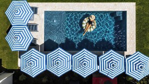 Ein Schwimmbecken mit einer Person auf einem Luftmatratze, umgeben von blauen und weißen Streifen-Schirmen.