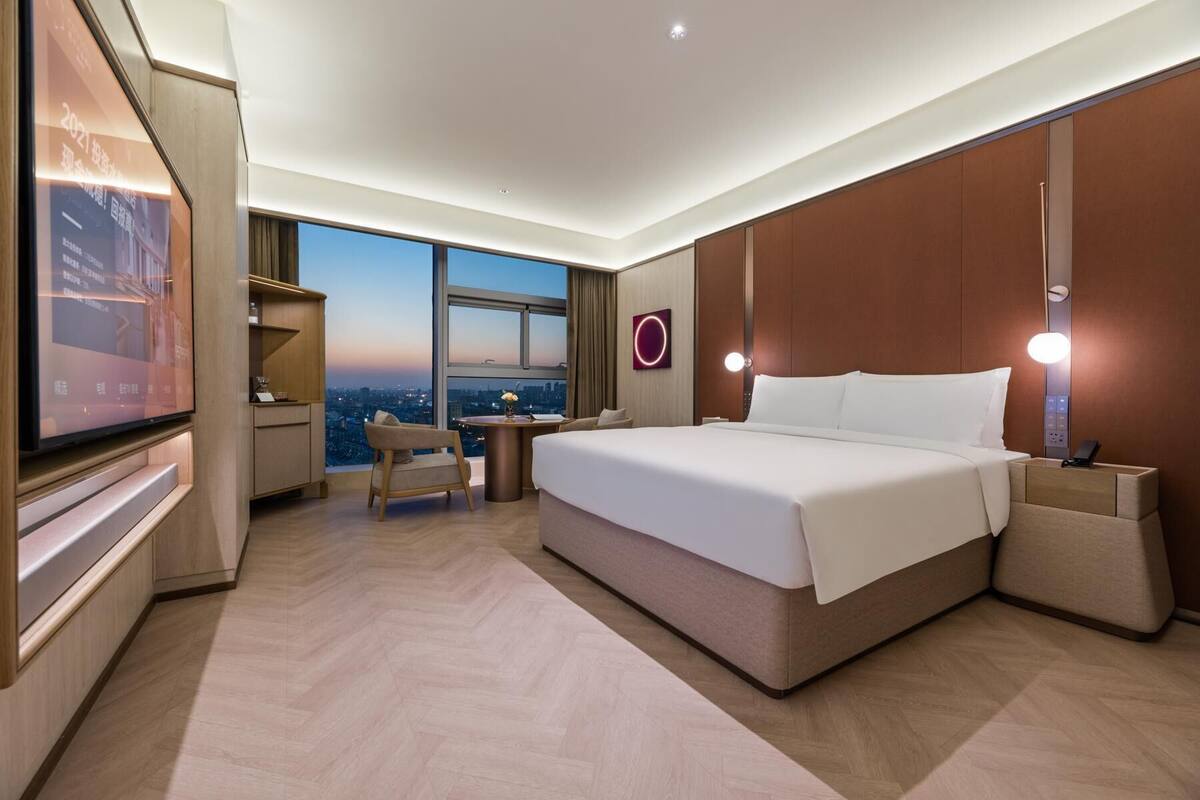 A modern hotel room with a large bed, a desk, a chair, and a television.