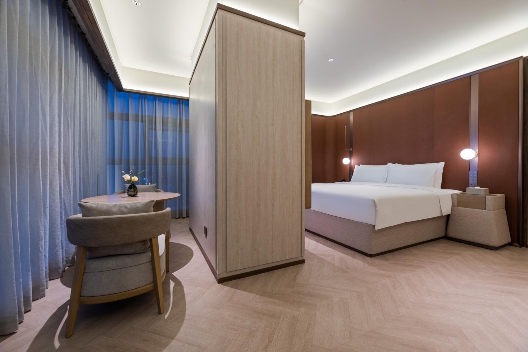 A hotel room with a bed, bedside table, and a small seating area with a chair and table.
