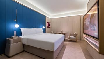 Habitación de hotel con una cama grande, mesitas de noche, un escritorio, una silla, un televisor y una obra de arte colgada en la pared.