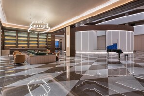 A spacious lobby with a checkered floor, a grand piano, a seating area with sofas, and a wall with illuminated shelves. - Crystal Orange Hotel Haimen Wenfeng Great World (Nantong)