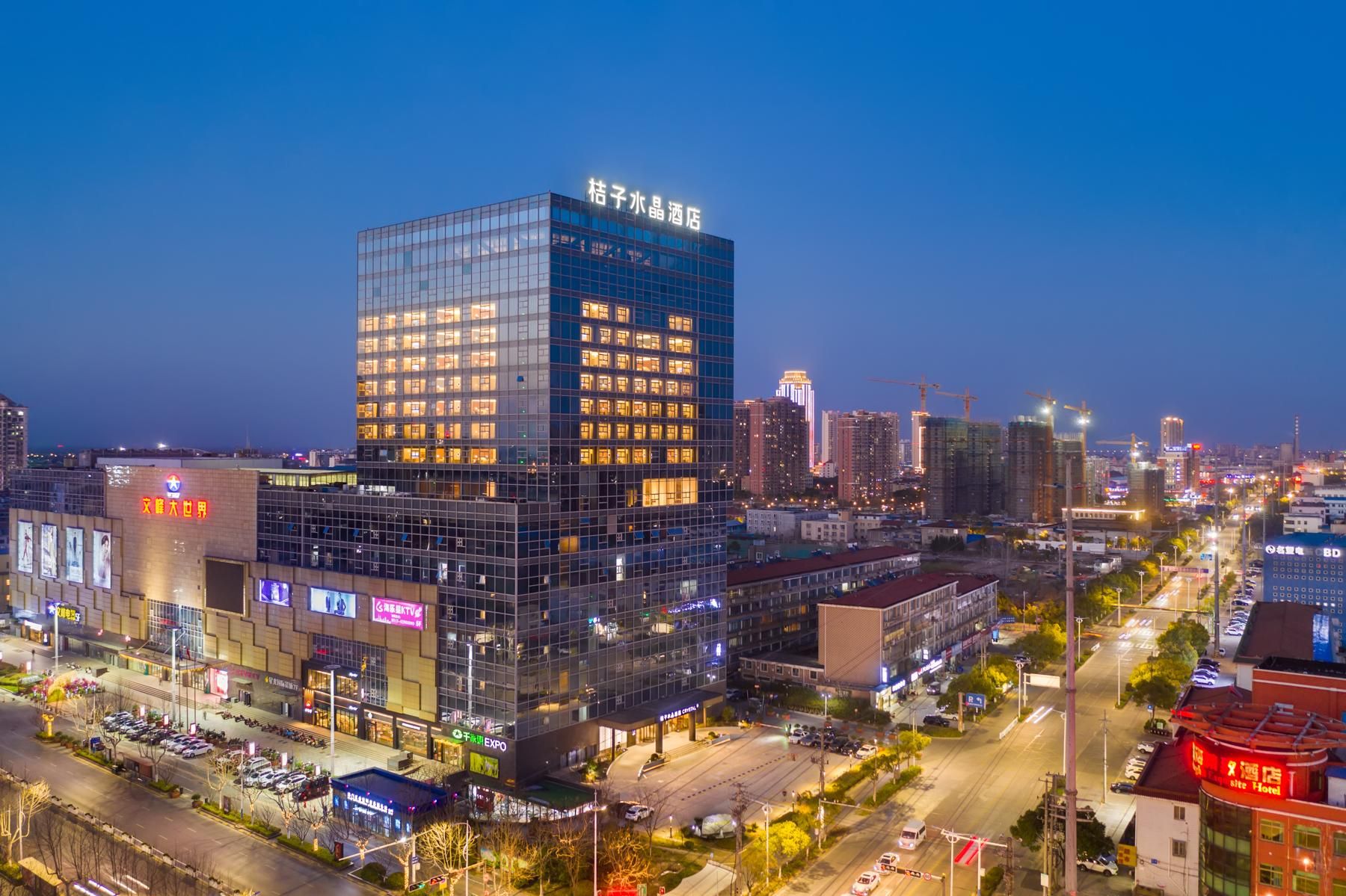 A modern hotel with a glass facade, located in a busy urban area with other buildings and a clear sky.