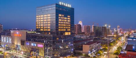 A modern hotel with a glass facade, located in a busy urban area with other buildings and a clear sky.