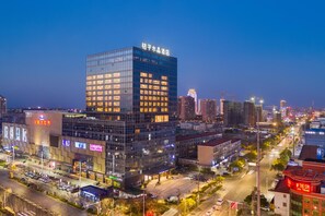 A modern hotel with a glass facade, located in a busy urban area with other buildings and a clear sky. - Crystal Orange Hotel Haimen Wenfeng Great World (Nantong)