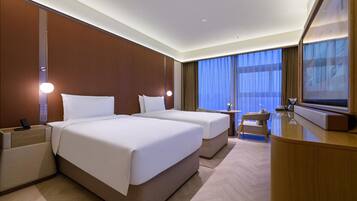 A hotel room with two beds, a desk, a chair, a television, and a large window with curtains.