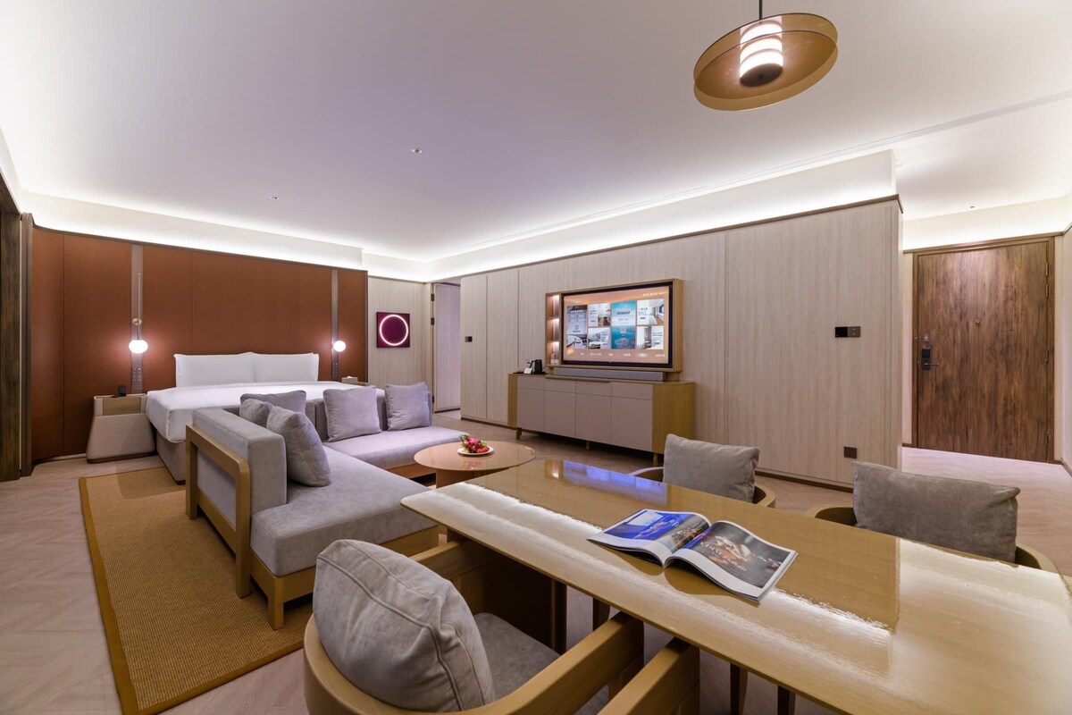 A modern hotel room with a sofa, a dining table, a TV, and a wooden cabinet.