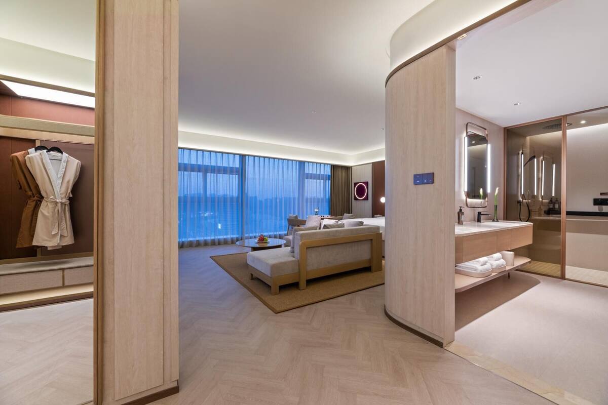 A modern hotel room with a large bed, a sitting area, and a bathroom with a mirror and sink.