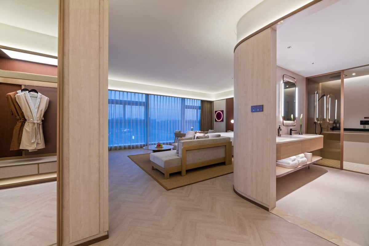 Quarto de hotel moderno com uma cama grande, um espaço de estar e um banheiro com espelho e pia.