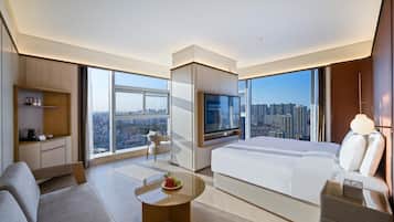 A modern hotel room with a large bed, a TV, a sofa, a coffee table, and a city view.