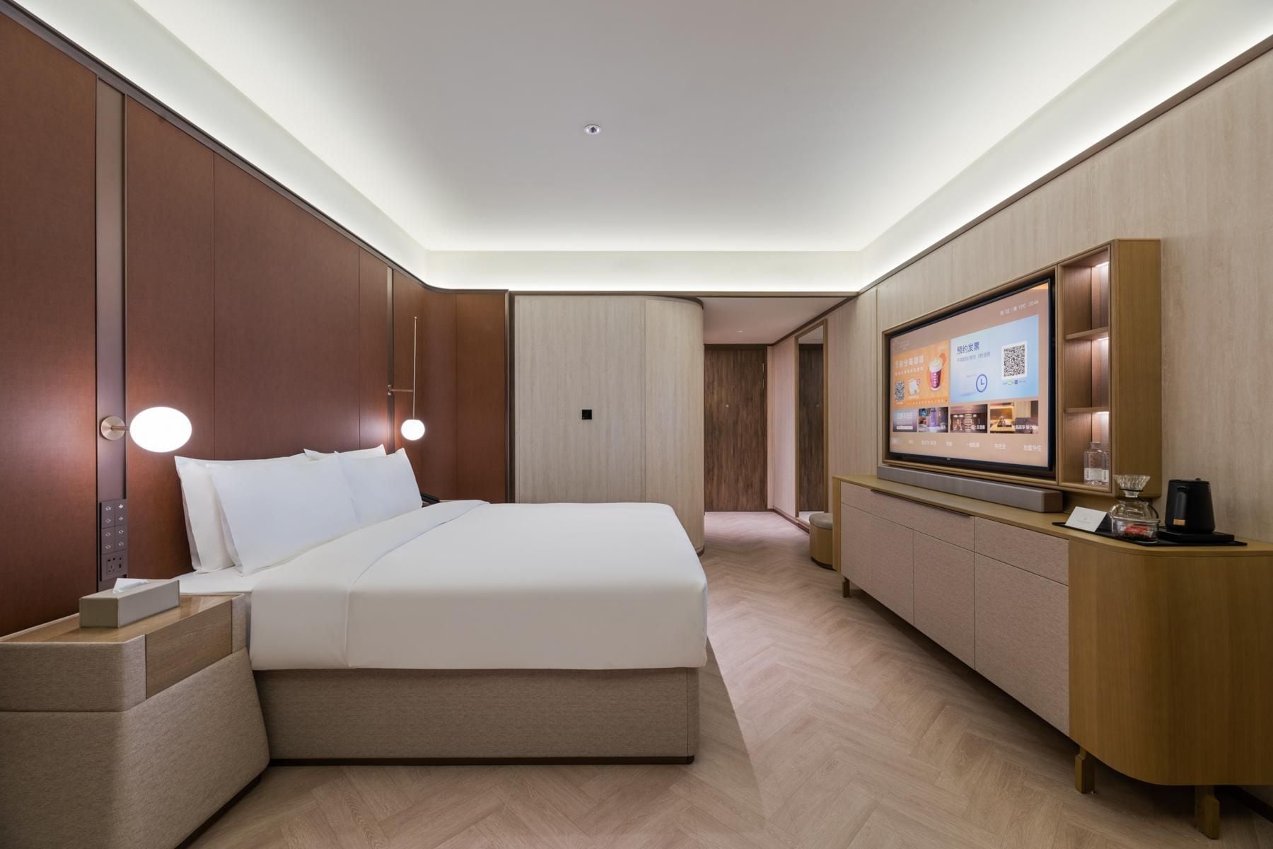 Una habitación de hotel moderna con una cama grande, televisión de pantalla plana, mesita de noche y minibar integrado.