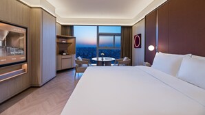 A hotel room with a large bed, a desk, a chair, a small table with a vase, and a view of the cityscape. - Crystal Orange Hotel Haimen Wenfeng Great World (Nantong)