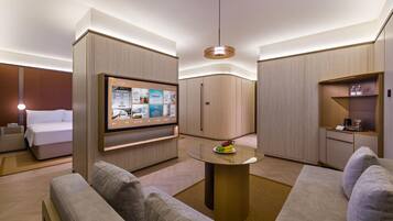 Una habitación de hotel moderna con una cama, un televisor montado en la pared, una mesa redonda con fruteros y un sofá.