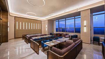 Un espace repas moderne avec des banquettes, un long comptoir et une vue sur le paysage urbain grâce à de grandes fenêtres.