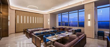 A modern dining area with booths and tables, large windows with a view, and contemporary lighting fixtures.