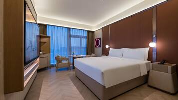 Une chambre d’hôtel moderne avec un grand lit, un bureau et une chaise. Il y a un téléviseur sur le côté gauche et un luminaire fixé au mur au-dessus du lit.